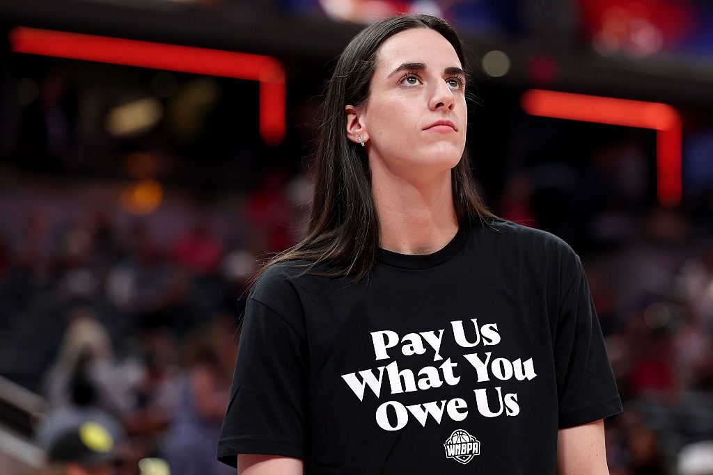Caitlin Clark (#22) of the Indiana Fever wears a shirt saying, "Pay us what you owe us"  